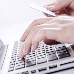 A person holding a credit card in one hand and typing with their other hand.